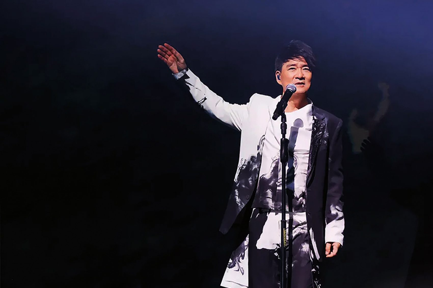 Wakin Chau standing on stage with his arm raised