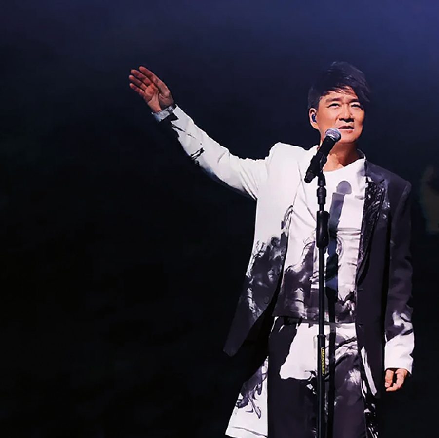 Wakin Chau standing on stage with his arm raised