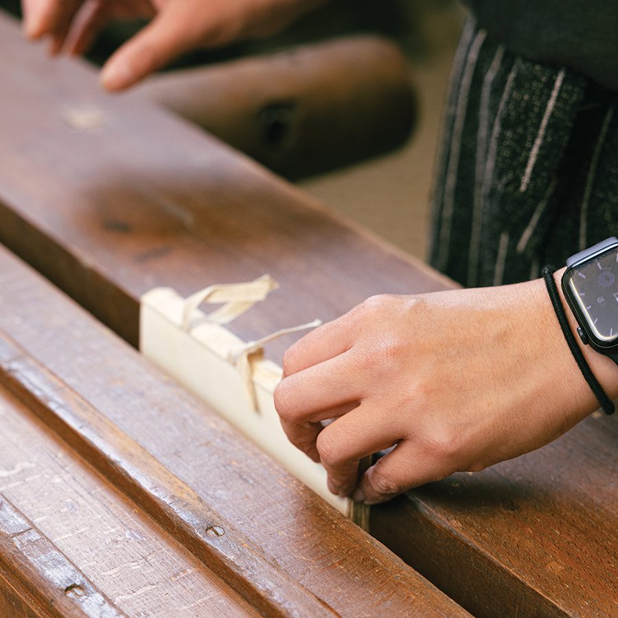A close-up of bookbinder Percy So using a wooden finishing press to clean and tile the spine of a book during repair 