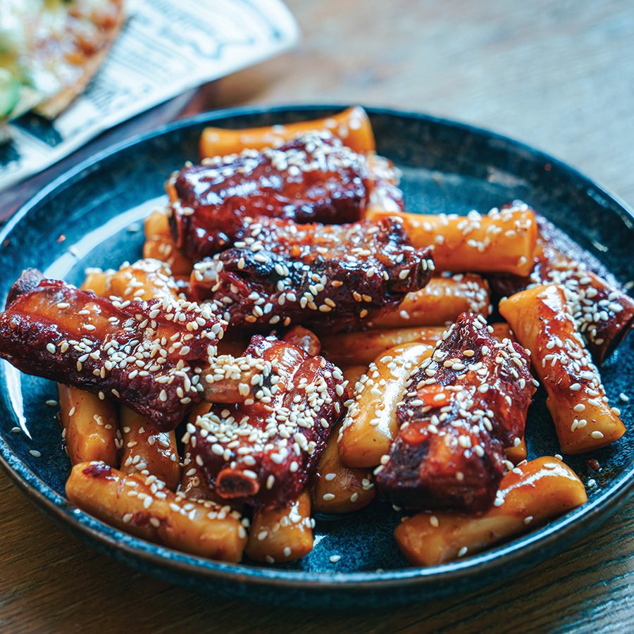 A close-up of Chinese rice rolls in sauce topped with sesame seeds on a black plate