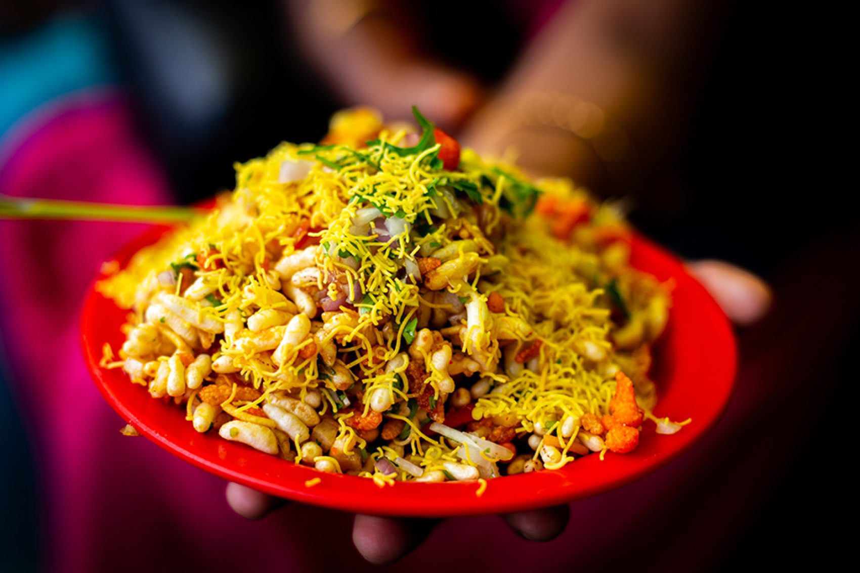 A closeup of a person holding a plate of bhelpuri puffed rice in tamarind sauce