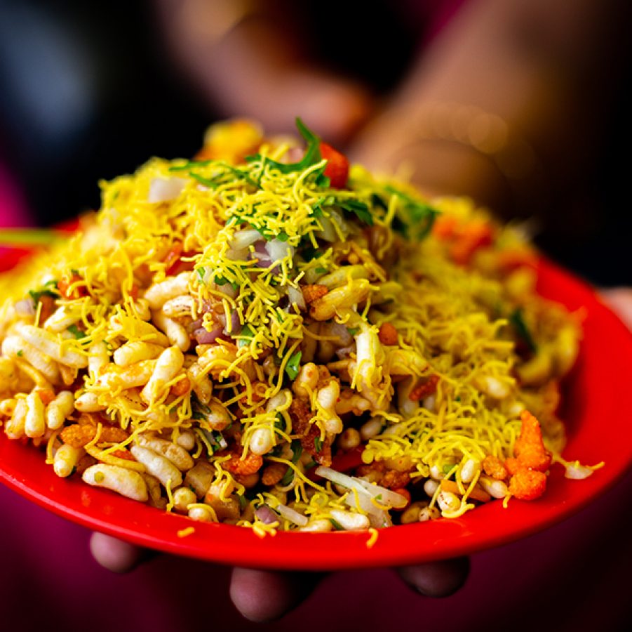 A closeup of a person holding a plate of bhelpuri puffed rice in tamarind sauce