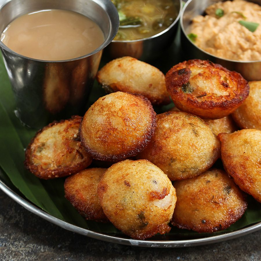 Paddu puffed dosa snack served with three types of dipping sauces on a green plate 