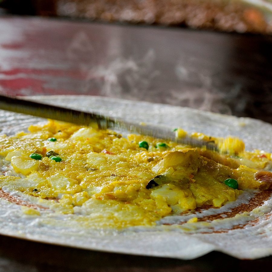 A close of up a masala dosa filled with spiced potato mash on a flat top grill 