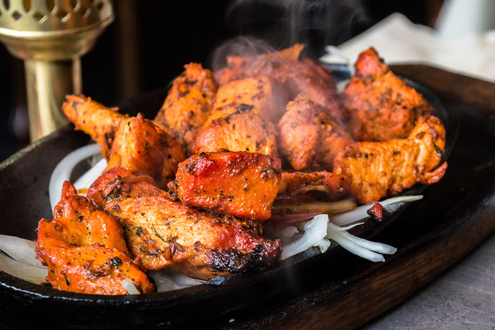 A platter of sizzling tandoori chicken served ontop of onions on a black iron plate    