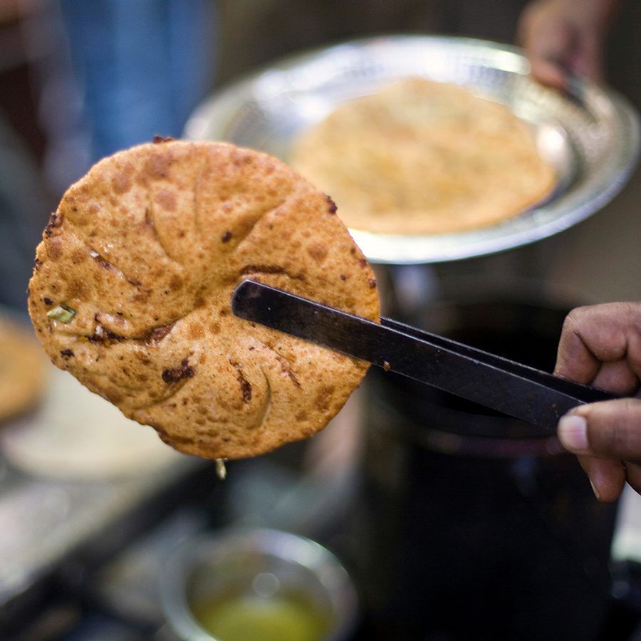 A close-up of an Indian street food vendor holding a paratha 