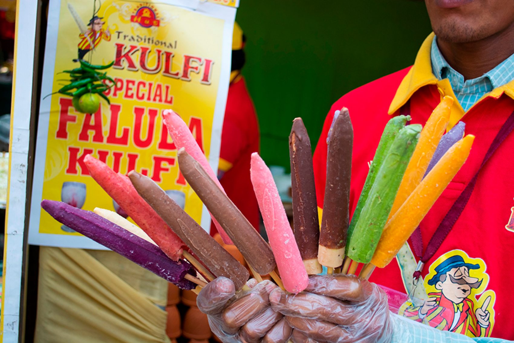 An Indian street food vendor holding sticks of kulfi in a variety of flavours