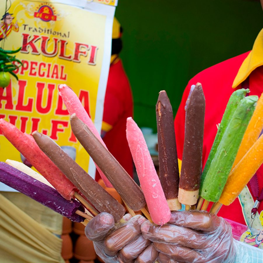 An Indian street food vendor holding sticks of kulfi in a variety of flavours