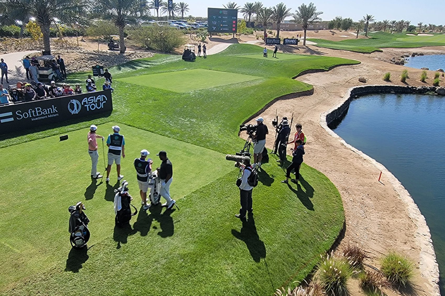 Golfers standing on grass and being filmed by a crew while spectators look on at Safaa Golf Club