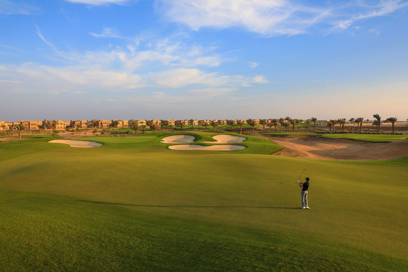 A person playing golf under blue skies at Royal Greens Golf & Country Club