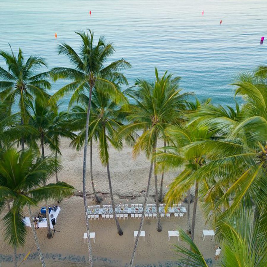 A long table and chairs surrounded by palm trees on the beach at Nu Nu. 
