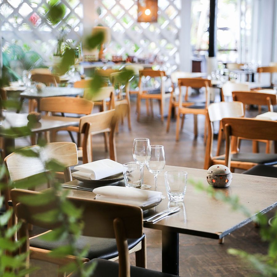 Wooden dining tables and chairs at Nu Nu, with plants in the foreground. 
