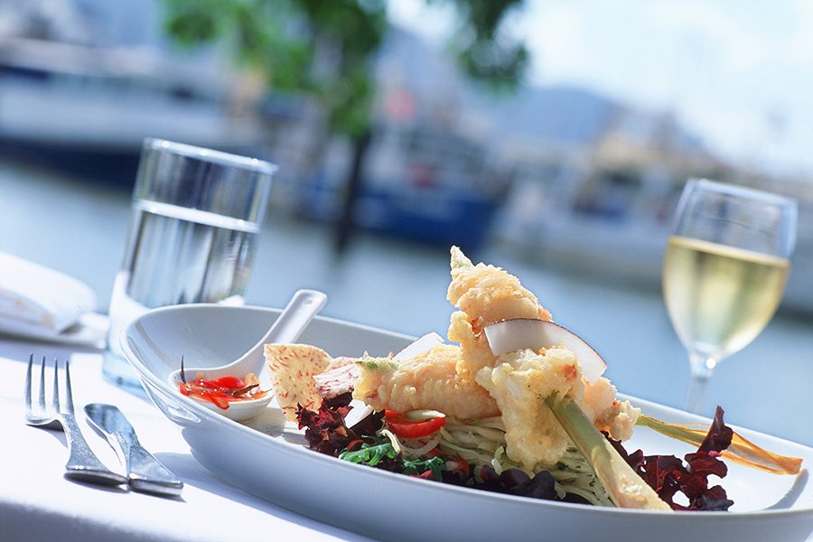 A plate of tempura and salad on a white tablecloth. There is a fork and knife next to the plate and a glass of water and white wine behind it.