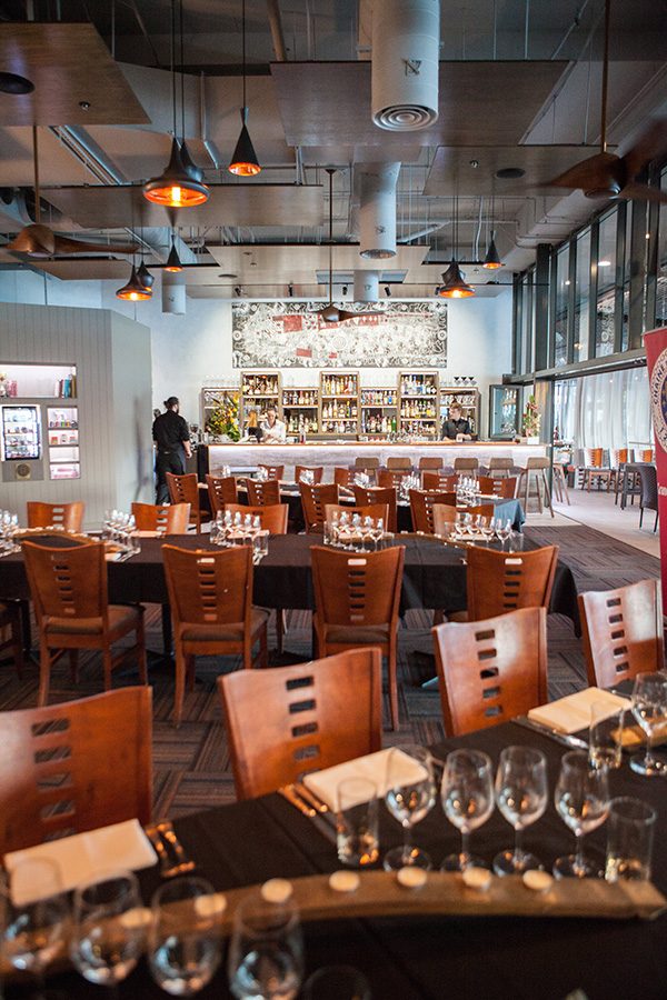The interior of Ochre with wooden chairs, glasses and black tablecloths on the tables, and a piece of artwork behind the bar.