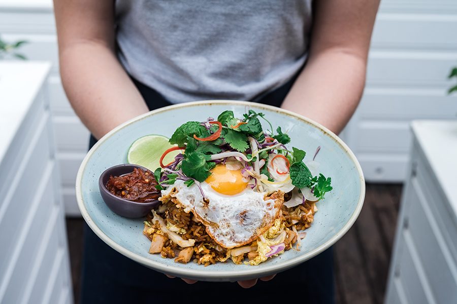 A plate of fried rice topped with a fried egg and salad, and a lime and a bowl of sauce on the side. 