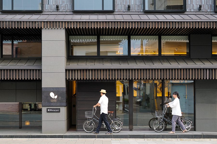Two people with bicycles pass the exterior of hotel Dhawa Yura Kyoto