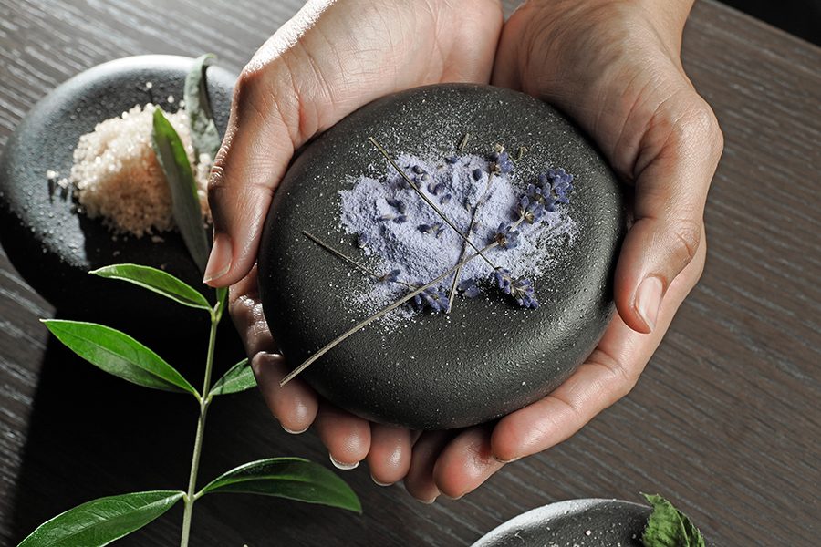 Hands hold a black stone with lavender and salt on it, at Dhawa Yura Kyoto spa 