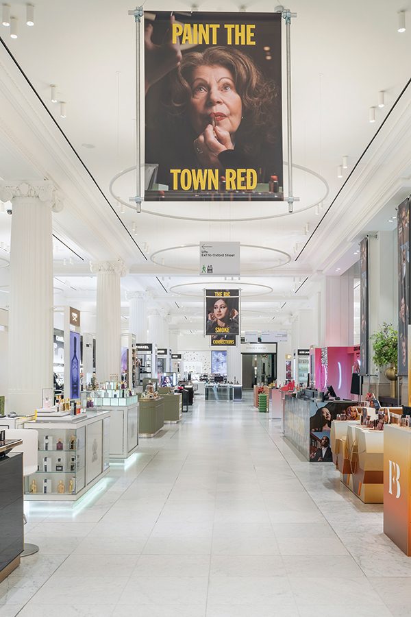 An interior shot of the beauty hall within Selfridges, London, with a banner hanging from the ceiling that says “paint the town red”