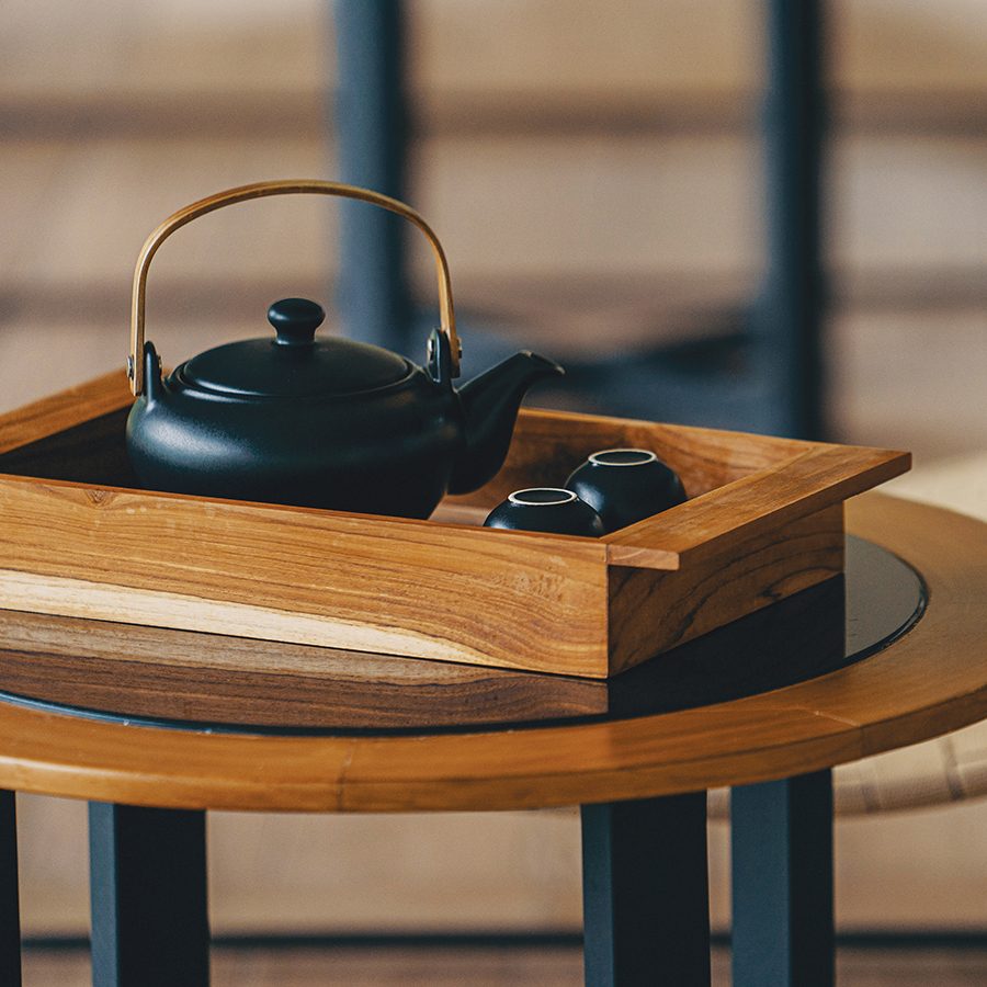 A small teapot and two teacups on a tray on a side table 