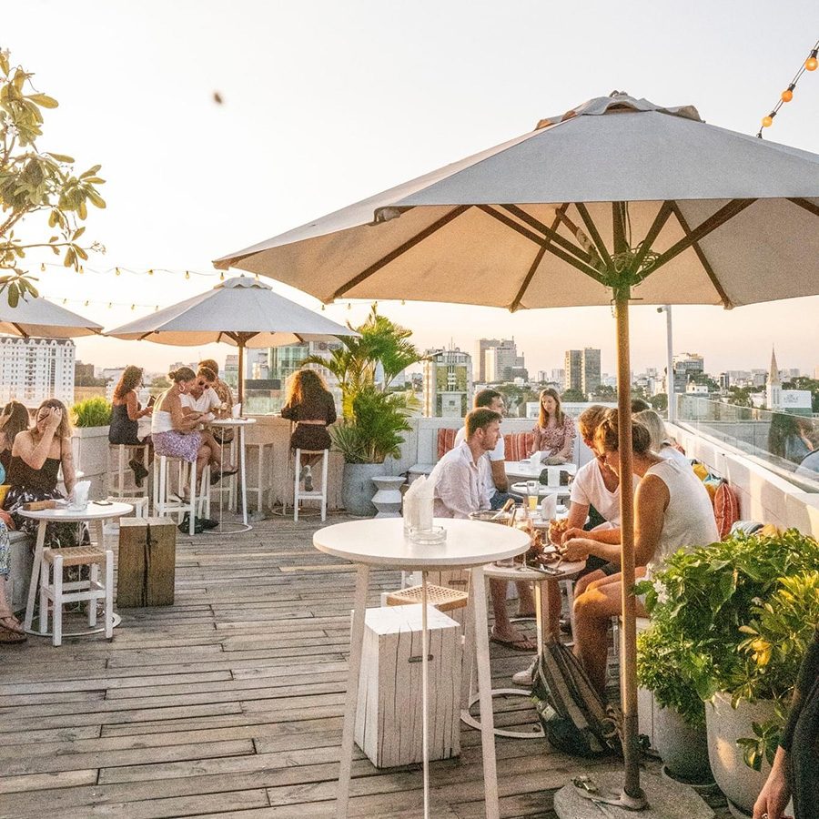 People enjoying cocktails at the alfresco dining area of Banana Mama Rooftop & Kitchen during a warm afternoon.