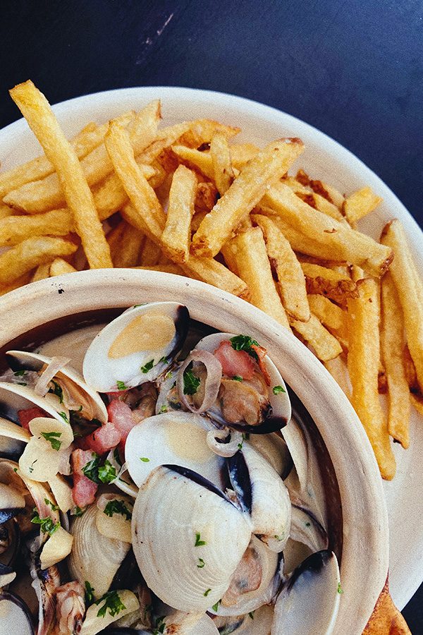 A top down closeup shot of a bowl of clams and a plate of french fries served at Le Cafe de Stagiaires. 