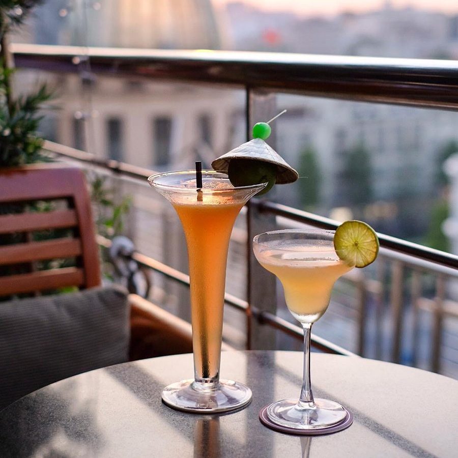 A portrait shot of two cocktails, Miss Saigon and a refreshing lime drink in a margarita glass, served at Saigon Saigon Rooftop Bar. 