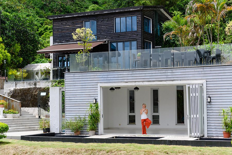 A woman in a one-legged yoga pose, standing inside a villa surrounded by greenery. 