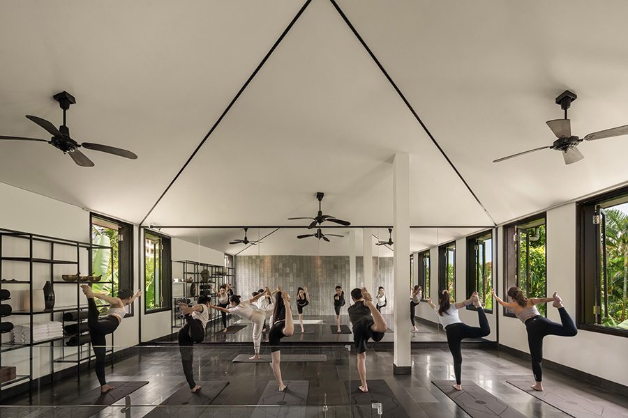 A group of people doing one-legged yoga poses on mats in a bright room with many windows.