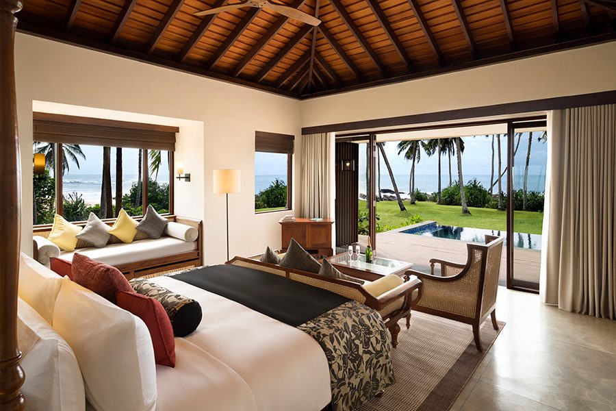 A hotel room with a bed and sofas inside and a pool outside.