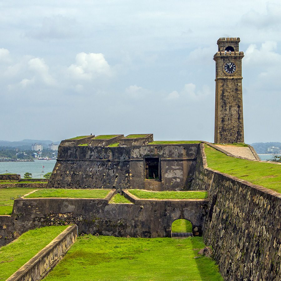 A stone clock tower and grass-covered cobbled pathways. 
