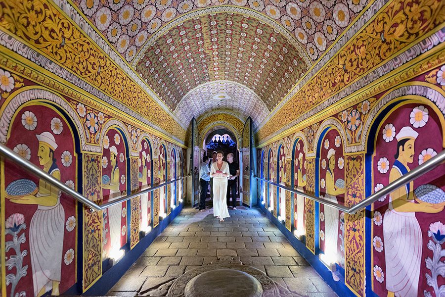 A group of people walking down a colourful patterned hallway in a temple. 