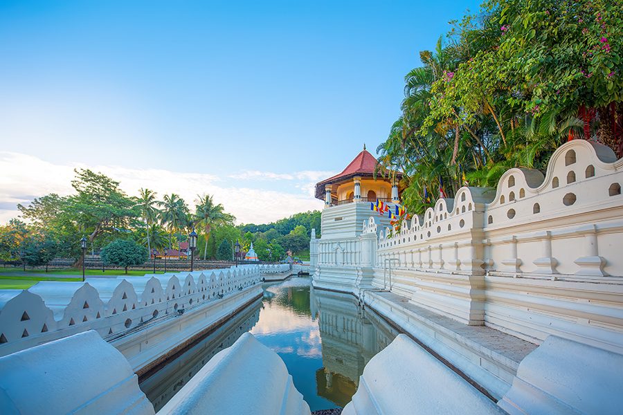A white temple with a red roof surrounded by trees and a lake.