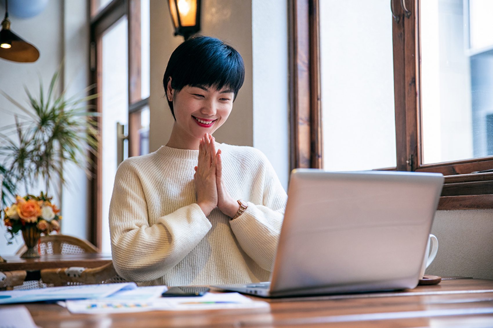 Woman with hands clasped as she looks at her laptop 