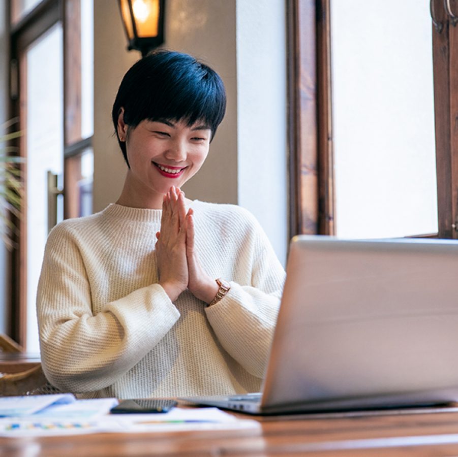 Woman with hands clasped as she looks at her laptop 