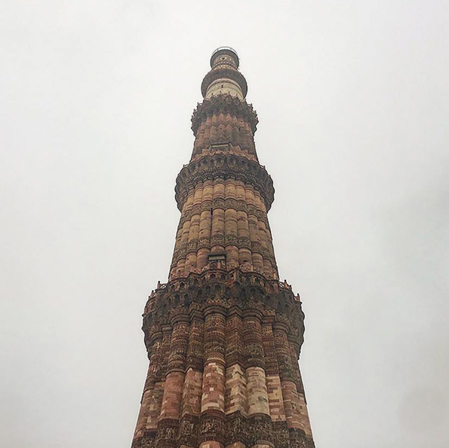 The Qutb Minar tower extending upward against a grey sky.