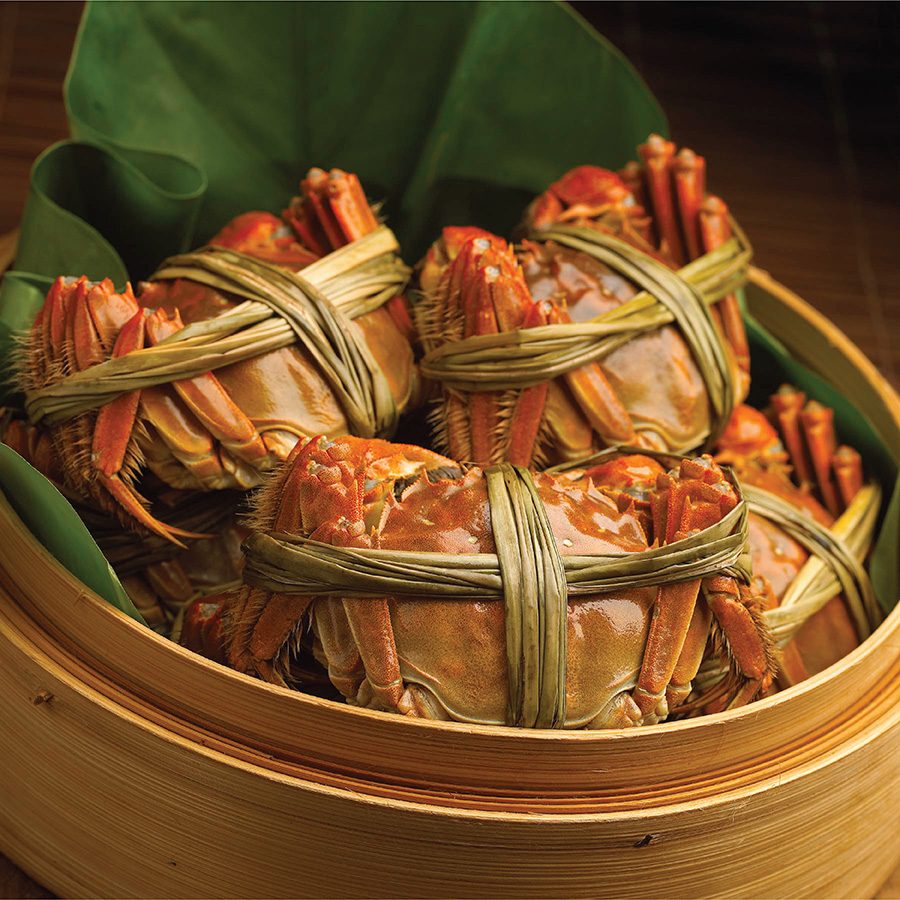 A bamboo steamer basket with four pieces of fresh hairy crab on a leaf served at T’ang Court in Tsim Sha Tsui, Hong Kong 