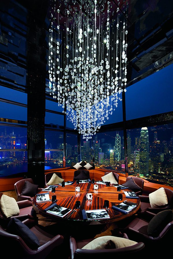 A corner table at Ozone, The Ritz-Carlton Hong Kong, with a chandelier above and the Hong Kong skyline at night visible through the windows.  