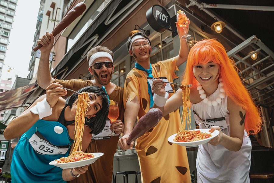 A group dressed as the Flintstones holds up pasta outside Pici for the Pici Pasta Run.