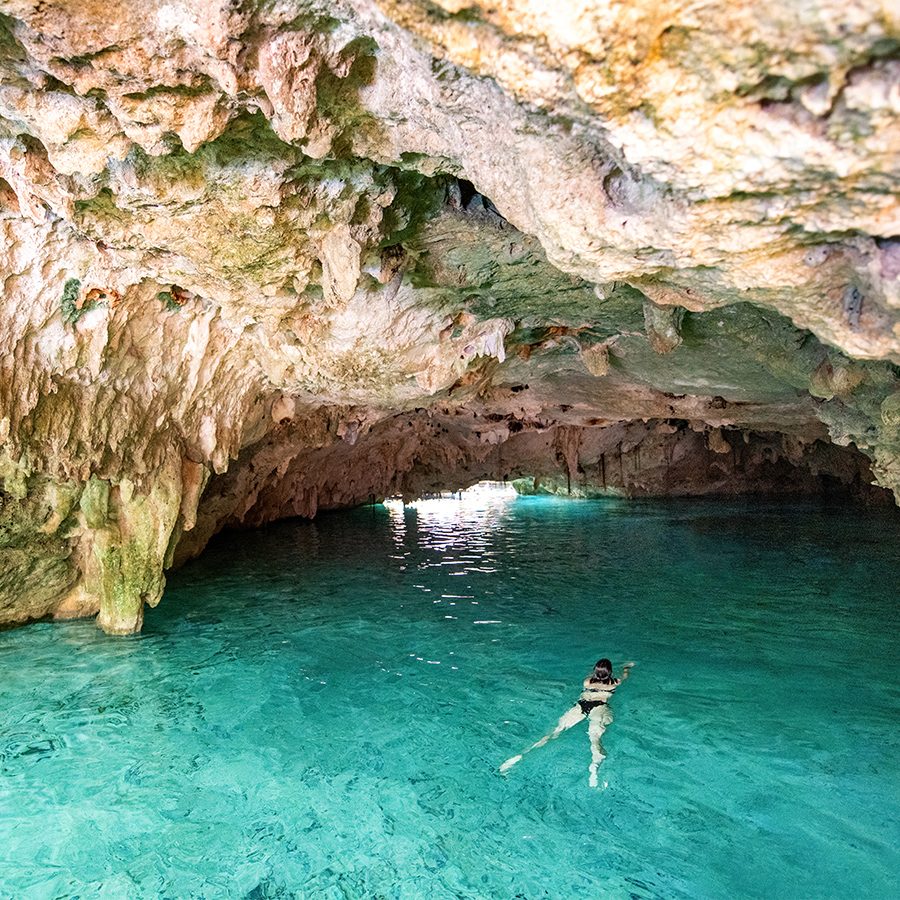 Woman swims through blue waters into a cave in Cancun.