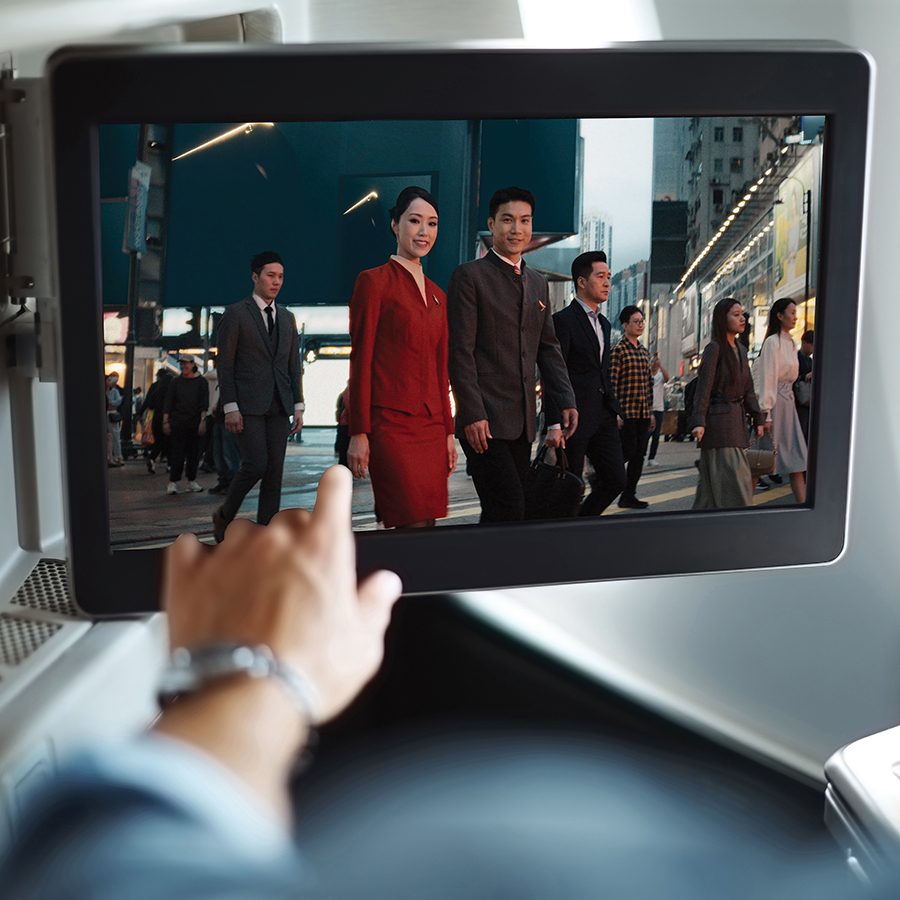 A hand reaching out to point at the inflight screen, which is showing Cathay Pacific’s new safety video starring two members of cabin crew, Cynthia Lam and Terry Lee.