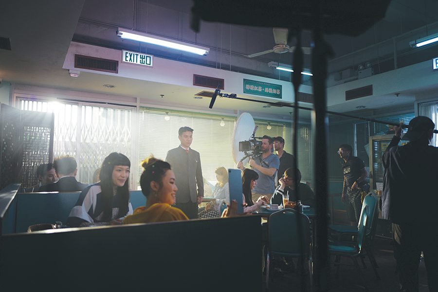 A group of actors and film crew on set in a dimly lit cha chaan teng. 