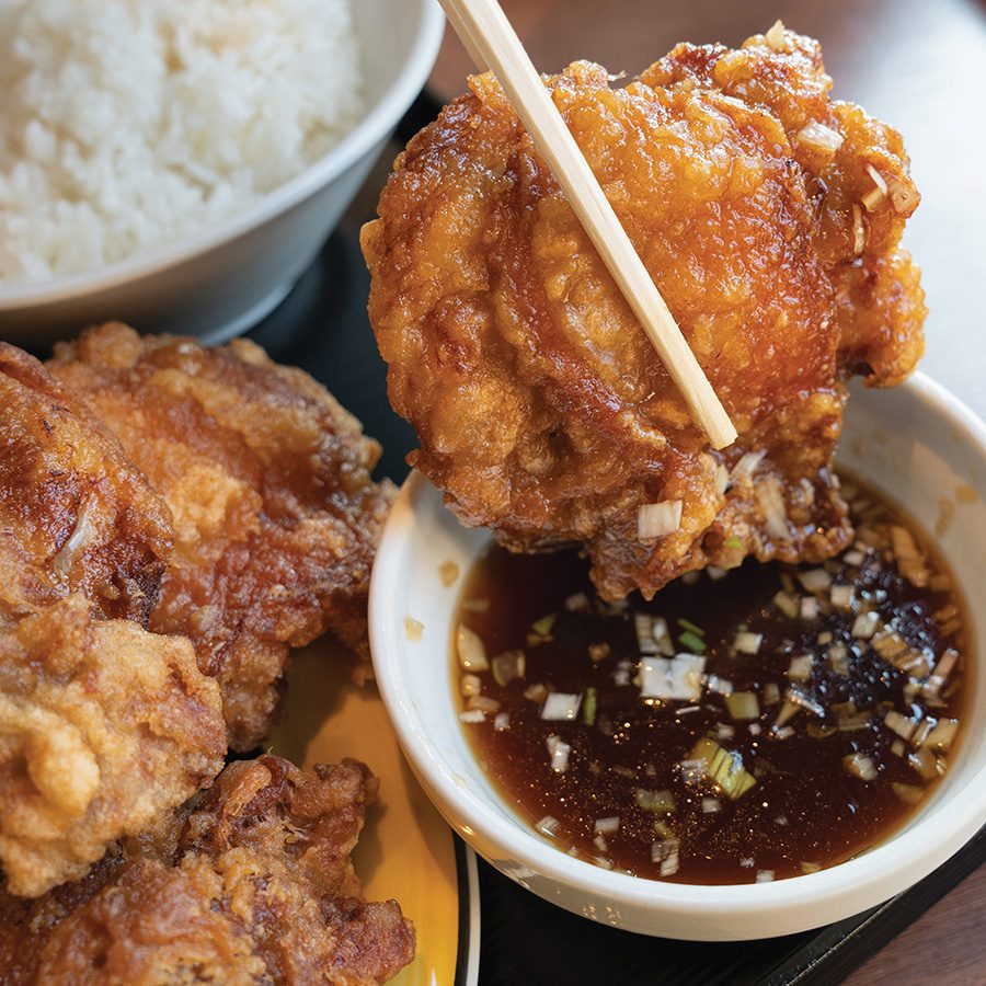 A close-up of a person dipping a piece of karaage Japanese fried chicken, served with with a bowl of white rice