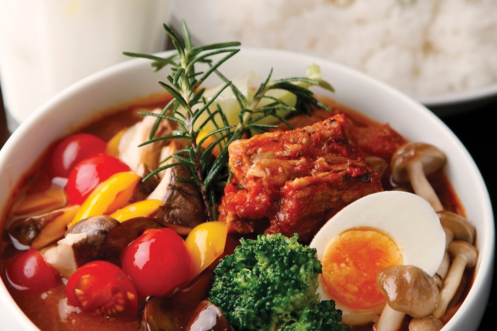 A close-up of a bowl of curry with mushroom, kimchi, tomato, egg and vegetables
