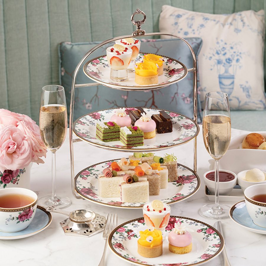 A three-tiered platter of finger treats from Palm Court’s afternoon tea set alongside cups of tea and champagne.