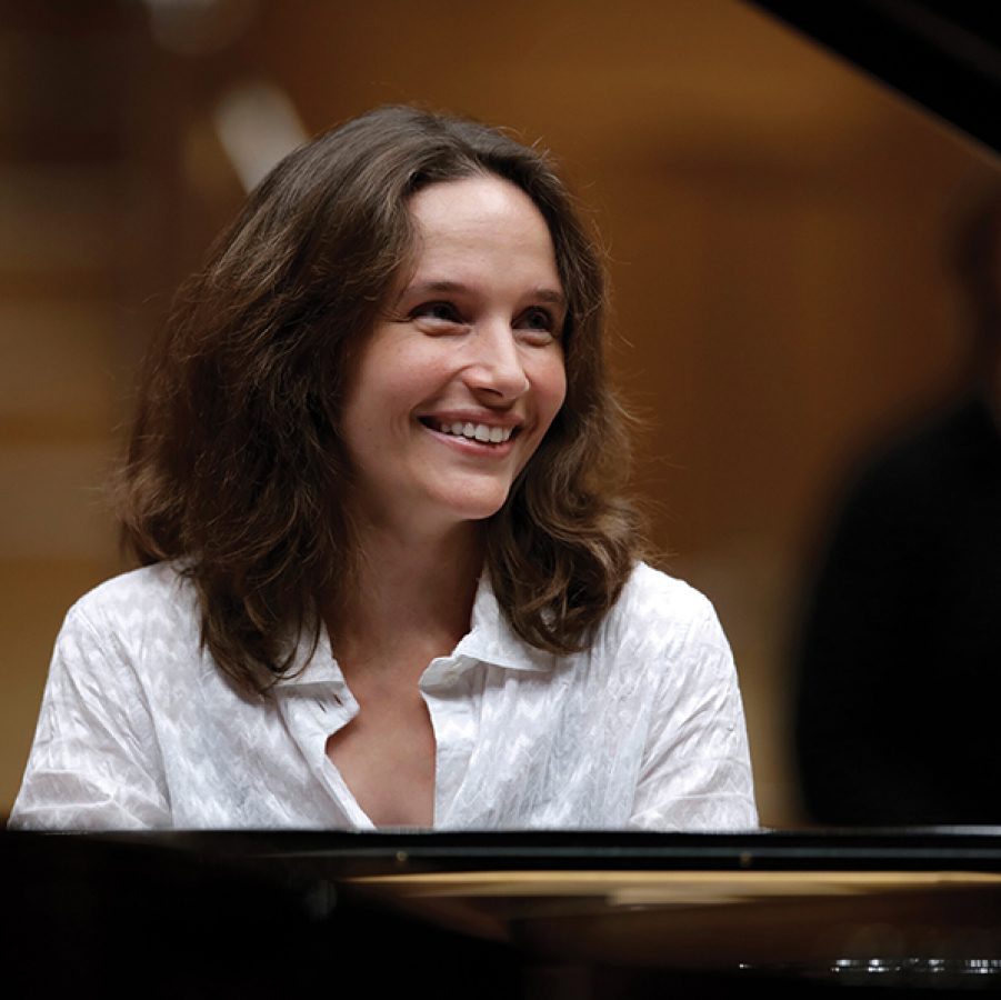 Close-up of French pianist Hélène Grimaud smiling while sitting behind a piano. 