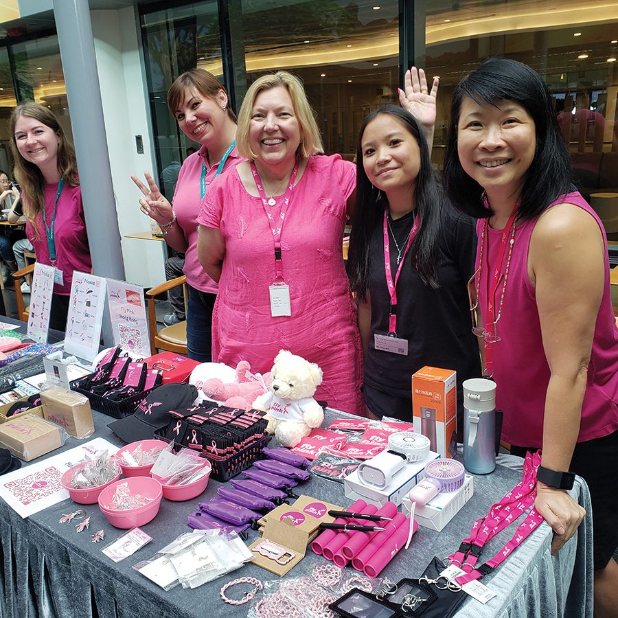 A group of women in pink standing next to a table selling items for breast cancer awareness. 