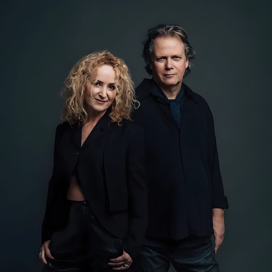 Violinist and singer Fionnuala Sherry and pianist Rolf Løvland of duo Secret Garden standing next to each other in front of a black backdrop. 