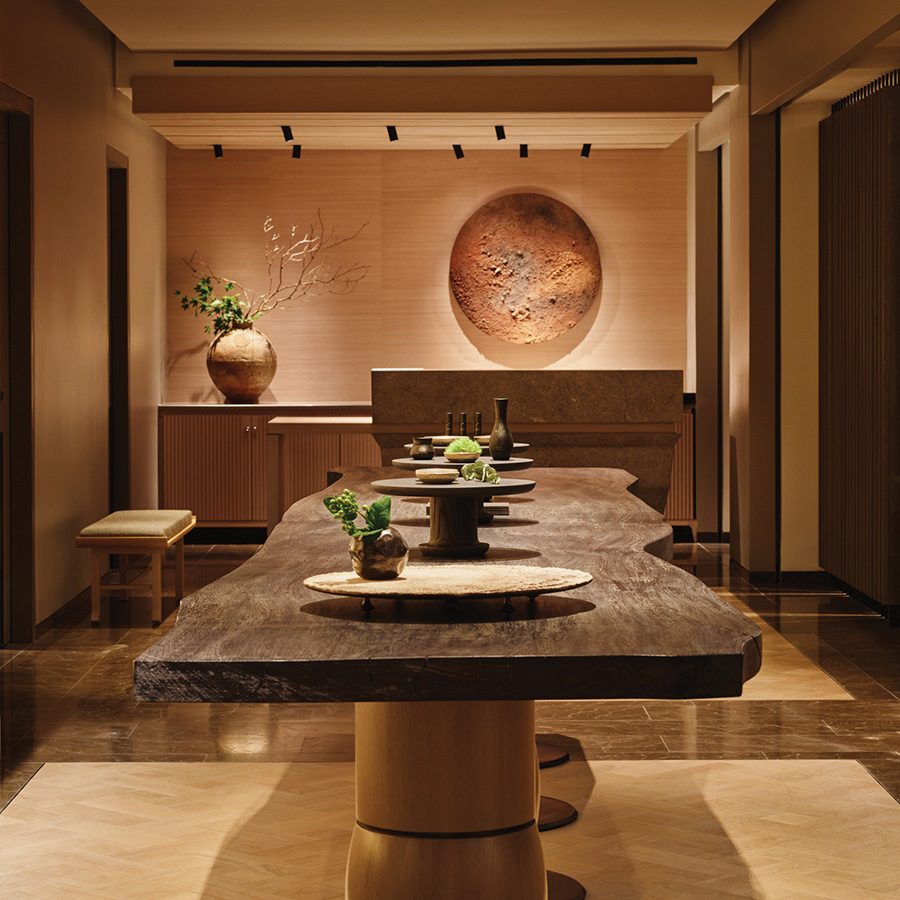 A long wooden table decorated with plants, in a neutral-coloured room 