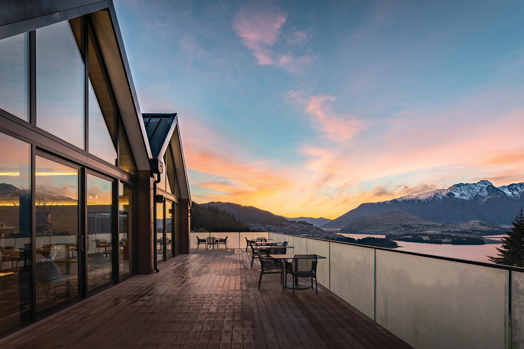 A long wooden deck overlooking a lake. In the distance, the sun sets behind mountains 