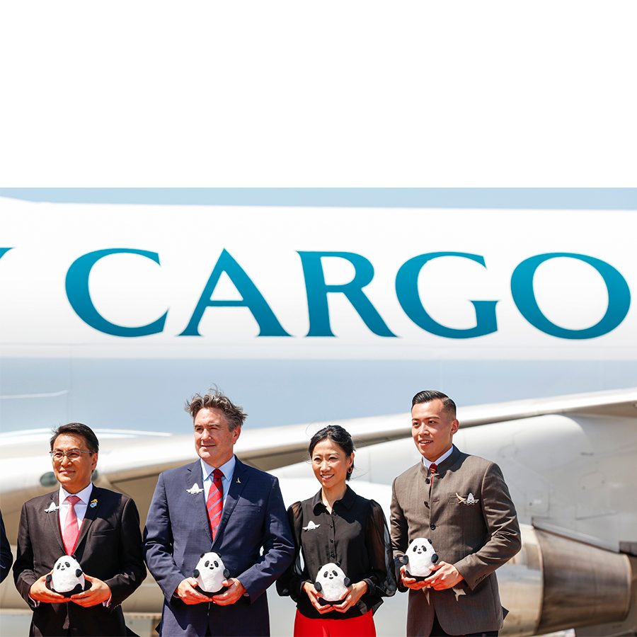Four people hold up stuffed toy pandas in front of the Cathay Cargo logo and plane